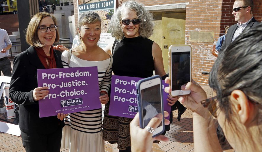 In this photo taken Oct. 17, 2018, Oregon Gov. Kate Brown, left, poses for photos with supporters after a rally in Portland, Ore. A measure to ban the use of state funds to pay for abortions is on the ballot in Oregon, the state with the least restrictive abortion laws in the nation. If it passes, Measure 106 would mean women who receive their health care through state Medicaid would not have insurance coverage for abortions. (AP Photo/Don Ryan)