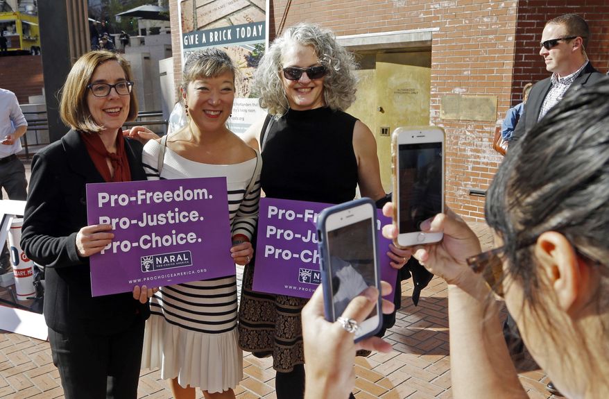 In this photo taken Oct. 17, 2018, Oregon Gov. Kate Brown, left, poses for photos with supporters after a rally in Portland, Ore. A measure to ban the use of state funds to pay for abortions is on the ballot in Oregon, the state with the least restrictive abortion laws in the nation. If it passes, Measure 106 would mean women who receive their health care through state Medicaid would not have insurance coverage for abortions. (AP Photo/Don Ryan)