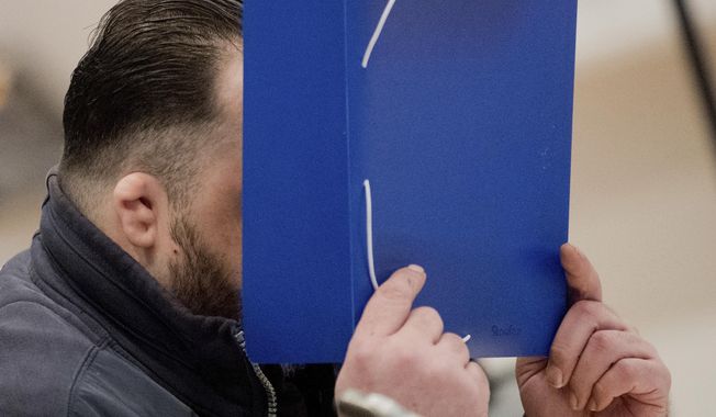The defandant covers his face with a folder as he arrives at the temporay Oldenburg district court at the Weser Ems halls in Oldenburg, Germany, Tuesday, Oct. 30, 2018. The nurse serving a life sentence for two murders is going on trial on charges that he killed a further 100 patients at two hospitals in Germany. (Julian Stratenschulte/dpa via AP, Pool)
