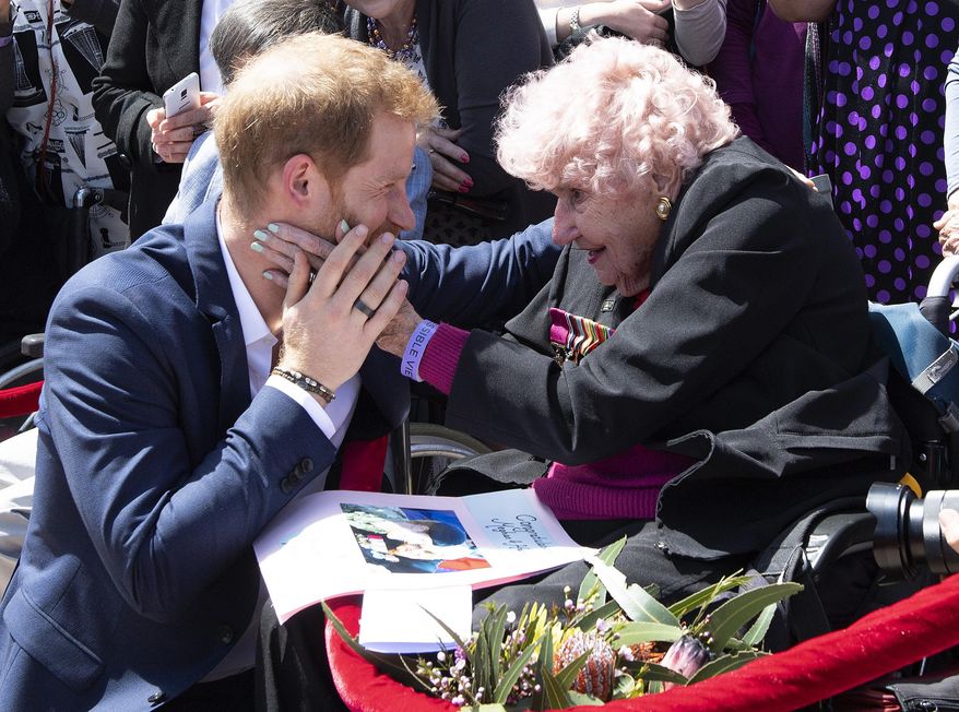 FILE- In this Oct. 16, 2018 file photo, Britain's Prince Harry is embraced by 97-year-old Dafney Dunne during a walk about outside the Opera House in Sydney, Australia. Prince Harry and his wife Meghan are on a 16-day tour of Australia and the South Pacific. (Paul Edwards/Pool via AP, File)