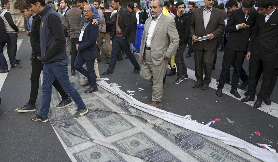 Demonstrators walk on a banner showing altered images of U.S. banknotes with a picture of President Donald Trump on the ground during a rally in front of the former U.S. Embassy in Tehran, Iran, on Sunday, Nov. 4, 2018, marking the 39th anniversary of the seizure of the embassy by militant Iranian students. Thousands of Iranians rallied in Tehran on Sunday to mark the anniversary as Washington restored all sanctions lifted under the nuclear deal. (AP Photo/Vahid Salemi)