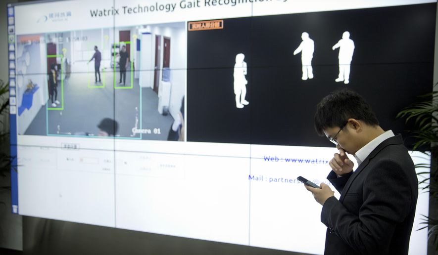 In this Oct. 31, 2018, photo, Huang Yongzhen, CEO of Watrix, checks his smartphone as employees demonstrate the use of their firm&#39;s gait recognition software at his company&#39;s offices in Beijing. A Chinese technology startup hopes to begin selling software that recognizes people by their body shape and how they walk, enabling identification when faces are hidden from cameras. Already used by police on the streets of Beijing and Shanghai, “gait recognition” is part of a major push to develop artificial-intelligence and data-driven surveillance across China, raising concern about how far the technology will go. (AP Photo/Mark Schiefelbein)