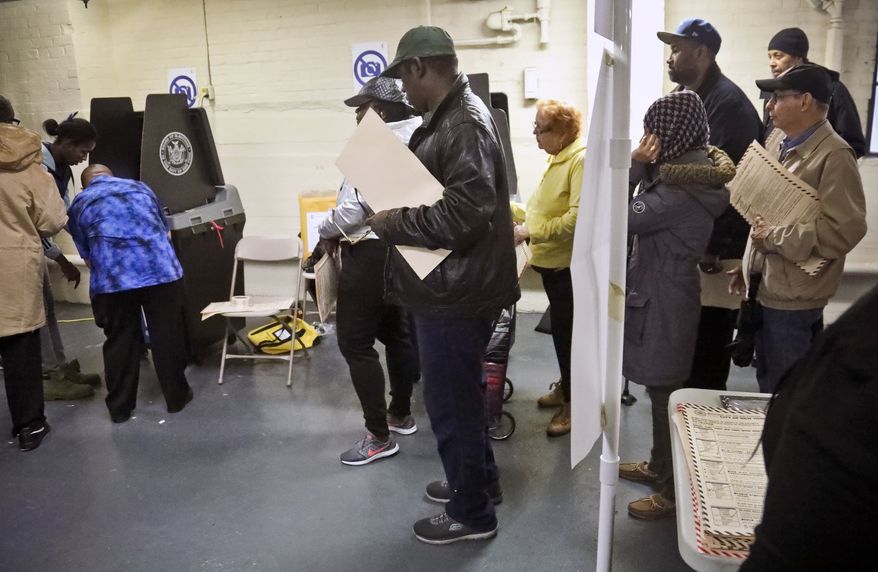 Polling site officials, left, check on a voting scanner after it jammed Tuesday, Nov. 6, 2018, in the Parkchester community of the Bronx borough of New York. The jam forced voters to manually file their ballots until a repair was made. (AP Photo/Bebeto Matthews)