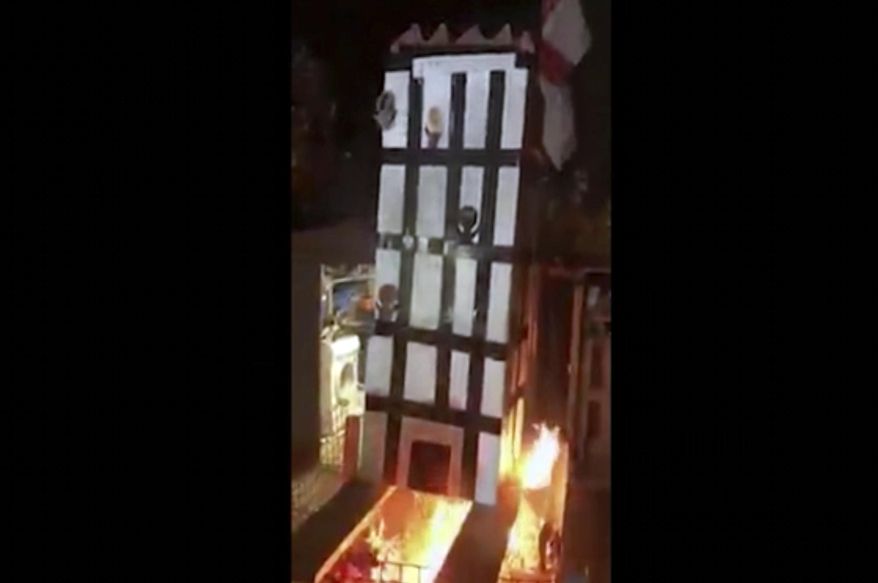 In this grab taken from video, made available on Tuesday, Nov. 6, 2018, people place a model of Grenfell Towers onto a bonfire, in London. London police have arrested five people over a video that showed a cardboard model of Grenfell Tower being burned on a bonfire — a video that shocked the families of the 72 victims who died in the 2017 inferno that engulfed the apartment block. (UGC via AP)