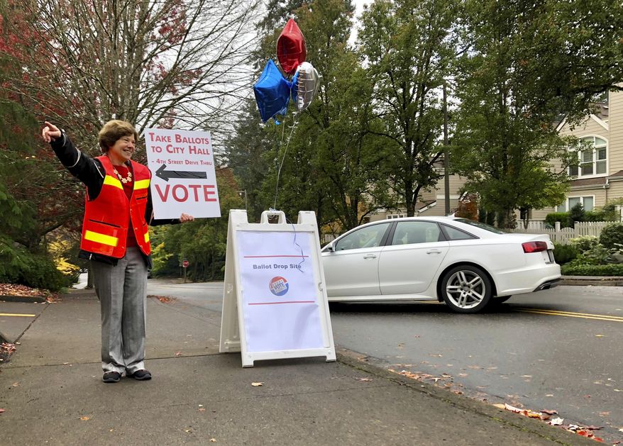 Elections volunteer Linda Brown points a voter to a designated ballot drop box in Lake Oswego, Oregon outside City Hall on Tuesday, Nov. 6, 2018. Brown said the dropbox location had been so busy that it was overflowing when elections workers emptied it Tuesday morning. Oregon is a vote-by-mail state and voters who have not mailed their ballots back by Election Day must deposit them in ballot boxes like this one. (AP Photo/Gillian Flaccus)