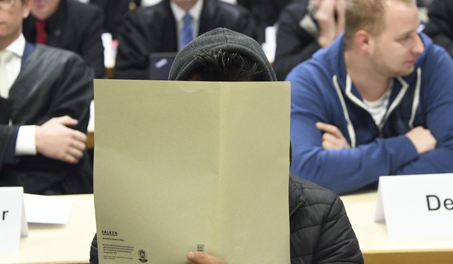 A defandant holds a folder to hide is face at a court in Siegen, Germany, Thursday, Nov. 8, 2018. The court is investigating accusations that guards at an asylum center in Burbach in western Germany repeatedly abused refugees physically and mentally. (Henning Kaiser/dpa via AP)