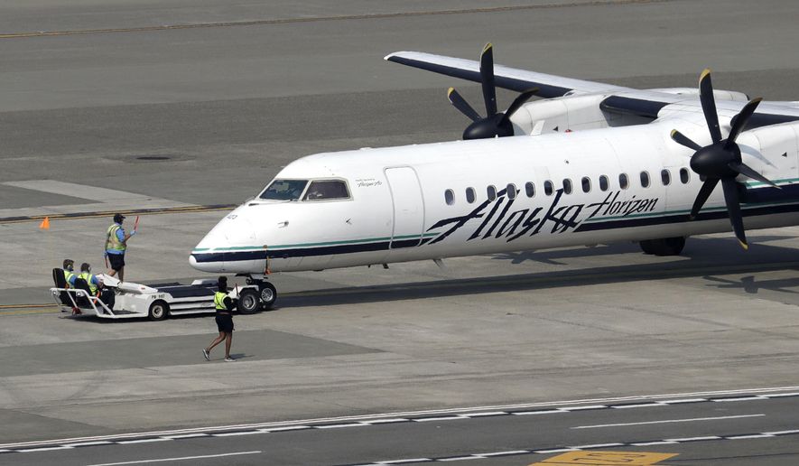 In this Aug. 13, 2018, file photo, a Horizon Air Q400 turboprop airplane, part of Alaska Air Group, is moved into position by airport workers at Seattle-Tacoma International Airport in SeaTac, Wash. (AP Photo/Elaine Thompson, File)
