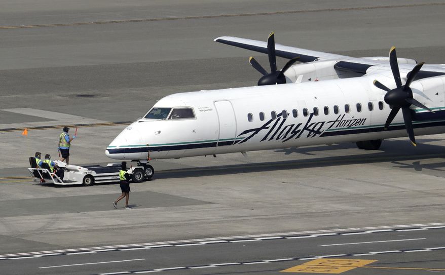 In this Aug. 13, 2018, file photo, a Horizon Air Q400 turboprop airplane, part of Alaska Air Group, is moved into position by airport workers at Seattle-Tacoma International Airport in SeaTac, Wash. (AP Photo/Elaine Thompson, File)