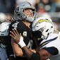Oakland Raiders quarterback Derek Carr (4) is hit between Los Angeles Chargers linebacker Uchenna Nwosu, left, and defensive tackle Corey Liuget during the first half of an NFL football game in Oakland, Calif., Sunday, Nov. 11, 2018. (AP Photo/John Hefti)