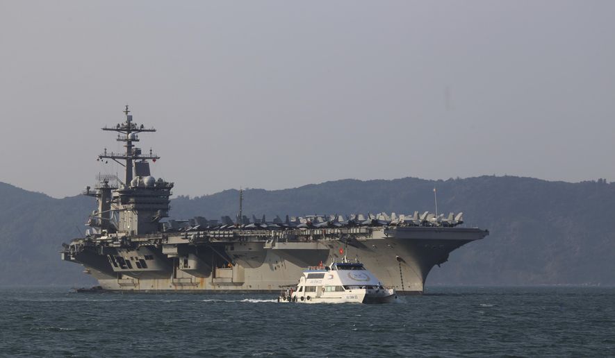 FILE - In this Monday, March 5, 2018, file photo, a Vietnamese passenger boat sails past U.S aircraft carrier USS Carl Vinson as it docks in Danang Bay, Vietnam. Over this last week, China demanded the United States stop sending ships and military aircraft close to its South China Sea island claims during talks to prepare for a meeting between President Donald Trump and President Xi Jinping later this month. (AP Photo/ Hau Dinh, File)