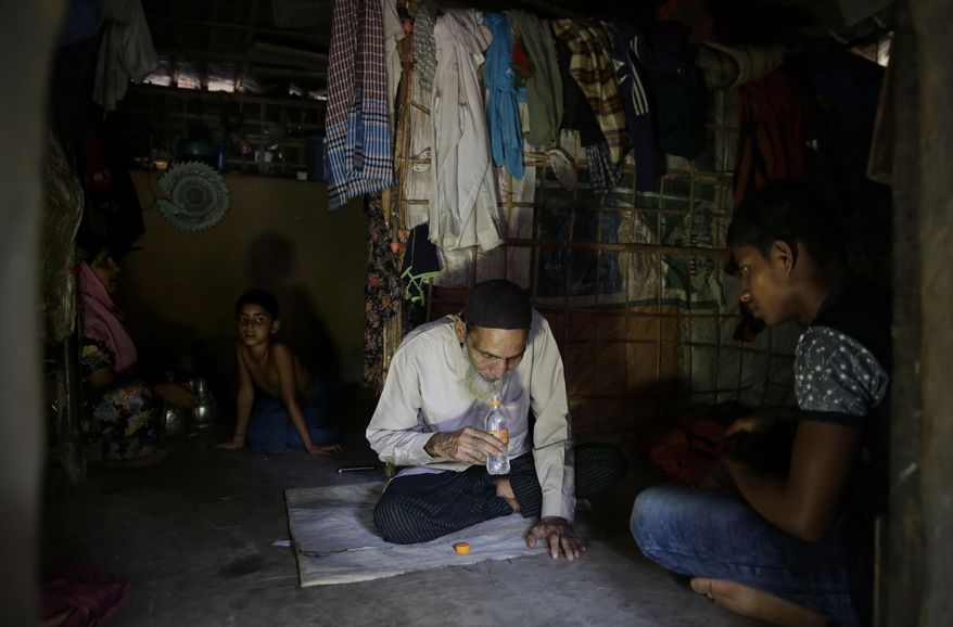In this photograph taken Aug. 24, 2018, Rohingya Rohingya faith healer Abul Kalam, left, whispers prayers into a water bottle for his patient, in Kutupalong refugee camp, Bangladesh. Access to medical care has changed for the better in the refugee camps in Bangladesh, yet many Rohingya still seek out their faith healers. (AP Photo/Altaf Qadri)