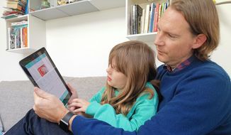 In this photo taken Oct. 21, 2018, Paddy Kelly and his daughter Ailish use Gohenry, one of a wave of digital banking apps for children, in London. A wave of digital pocket money apps that come with prepaid cards are new tools for financial education as money increasingly goes digital, in a shift that’s raising uncertainty about how cashless transactions affect youngsters’ view of money. (AP Photo/Kelvin Chan)