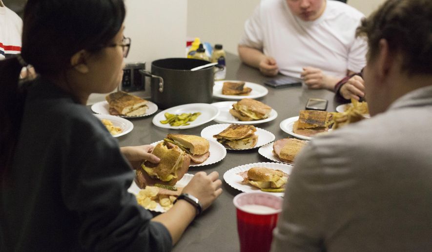 In this Wednesday, Nov. 7, 2018 photo, members of the University of Minnesota's Cooking Club gather outside the kitchen in Coffman Memorial Union to enjoy the meal they just prepared together in Minneapolis. A love of food, the social networking website Reddit and a persistent University of Minnesota graduate student, Justin Wiese, who wanted to create a space for people who like to eat were all factors in the creation of the university’s cooking club. (Jerusa Nyakundi/The Minnesota Daily via AP)