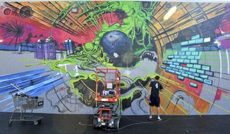 In this Oct. 8, 2018 photo, Bradley University student Mike Brown works on a mural  on the Unclaimed Freight store in Peoria, Ill. The new mural on the UFS Downtown Outlet Center is the largest piece of art the Bradley student has ever created. The brightly colored 20-foot by 50-foot mural draws upon Brown&#39;s love for science fiction and graffiti. (Leslie Renken/Journal Star via AP)