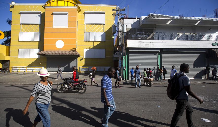 Residents walk past closed businesses on the third day of a strike and of countrywide protests over allegations of government corruption, in Port-au-Prince, Haiti, Tuesday, Nov. 20, 2018. Demonstrators are calling for the president to resign for not investigating allegations of corruption in the previous government over a Venezuelan subsidized energy program, Petrocaribe. (AP Photo/Dieu Nalio Chery)