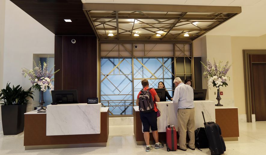 FILE- In this Sept. 5, 2018, file photo guests stand at the front desk at the Embassy Suites by Hilton hotel in Seattle's Pioneer Square neighborhood in Seattle. Automatic elite status in hotel loyalty programs is an increasingly common feature on credit cards associated with these programs. Now, some cards, such as the Starwood Preferred Guest Luxury Card and Hilton Honors American Express Aspire card, which both carry annual fees of $450, even give cardholders access to the upper echelons of elite status. (AP Photo/Ted S. Warren, File)