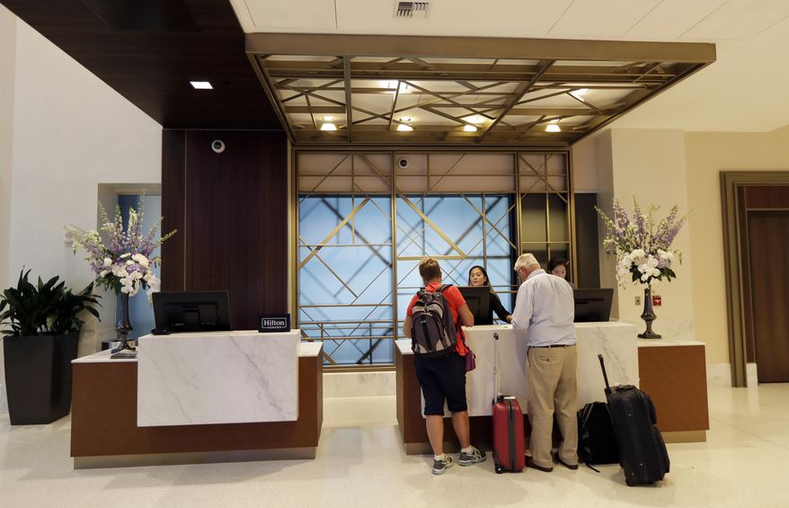 FILE- In this Sept. 5, 2018, file photo guests stand at the front desk at the Embassy Suites by Hilton hotel in Seattle's Pioneer Square neighborhood in Seattle. Automatic elite status in hotel loyalty programs is an increasingly common feature on credit cards associated with these programs. Now, some cards, such as the Starwood Preferred Guest Luxury Card and Hilton Honors American Express Aspire card, which both carry annual fees of $450, even give cardholders access to the upper echelons of elite status. (AP Photo/Ted S. Warren, File)