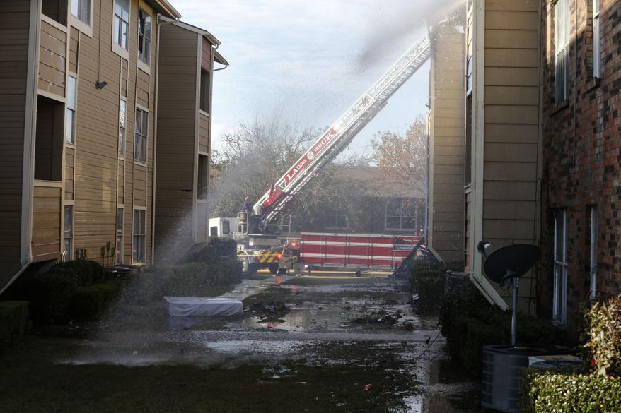 Firefighters put out hot spots during an apartment fire at the intersection of Interstate 635 and Ferguson Rd. in Dallas on Wednesday, Nov. 21, 2018. Some residents of a Dallas apartment complex leaped from third-floor windows onto mattresses, and a woman dropped her baby to a bystander to escape the flames. (Nathan Hunsinger/The Dallas Morning News via AP)