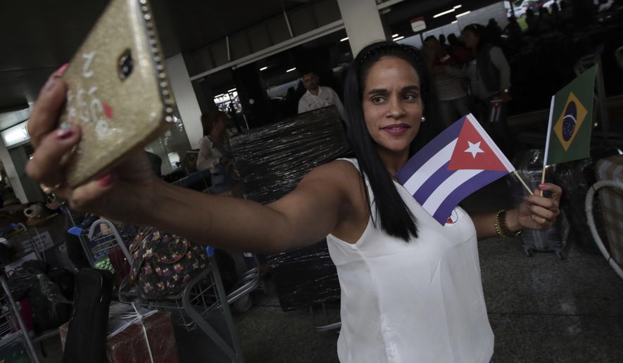 A Cuban doctor holding Brazilian and Cuban flags takes a selfie before she and other Cuban physicians return home at the airport in Brasilia, Brazil, Thursday, Nov. 22, 2018. Cuba announced it is recalling the physicians in the "More Doctors" program after Brazilian President-elect Jair Bolsonaro said the program could continue only if doctors get their full pay directly rather from the Cuban government and are able to bring their families with them. (AP Photo/Eraldo Peres)