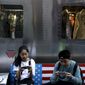 FIEL - In this Sept. 24, 2018, file photo, shoppers sit on a bench with a decorated with U.S. flag browsing their smartphones outside a fashion boutique selling U.S. brand clothing at the capital city&#39;s popular shopping mall in Beijing. China will go along with changes meant to update global trade rules but they must protect Beijing’s status as a developing country, a Cabinet official said Friday, Nov. 23, 2018. (AP Photo/Andy Wong, File)