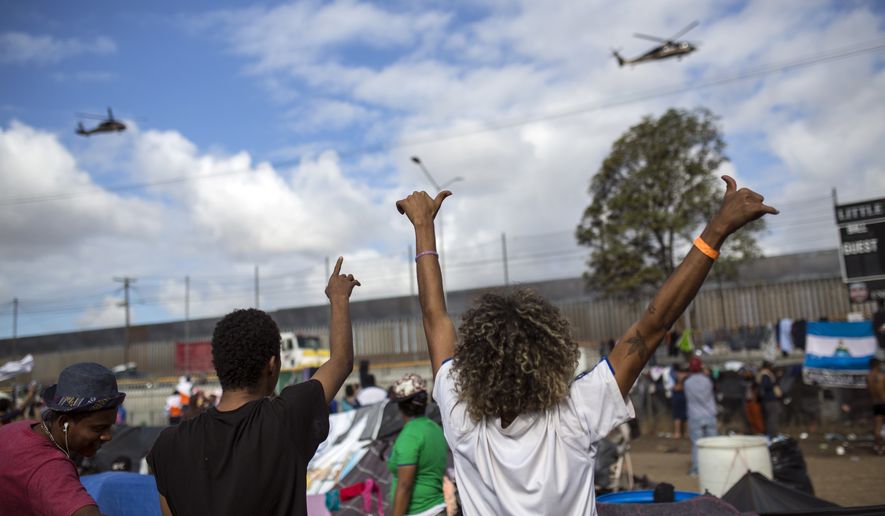 Migrants wave at U.S. border control helicopters flying near the Benito Juarez Sports Center serving as a temporary shelter for Central American migrants, in Tijuana, Mexico, Saturday, Nov. 24, 2018. The mayor of Tijuana has declared a humanitarian crisis in his border city and says that he has asked the United Nations for aid to deal with the approximately 5,000 Central American migrants who have arrived in the city.