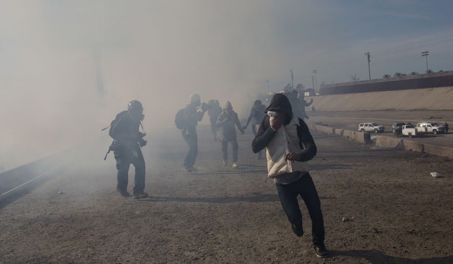 Migrants run from tear gas launched by U.S. agents, amid photojournalists covering the Mexico-U.S. border, after a group of migrants got past Mexican police at the Chaparral crossing in Tijuana, Mexico, Sunday, Nov. 25, 2018. The mayor of Tijuana has declared a humanitarian crisis in his border city and says that he has asked the United Nations for aid to deal with the approximately 5,000 Central American migrants who have arrived in the city.  (AP Photo/Rodrigo Abd)