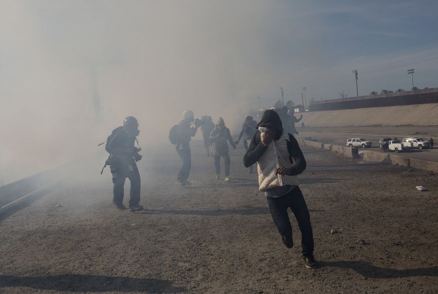 Migrants run from tear gas launched by U.S. agents, amid photojournalists covering the Mexico-U.S. border, after a group of migrants got past Mexican police at the Chaparral crossing in Tijuana, Mexico, Sunday, Nov. 25, 2018. The mayor of Tijuana has declared a humanitarian crisis in his border city and says that he has asked the United Nations for aid to deal with the approximately 5,000 Central American migrants who have arrived in the city.  (AP Photo/Rodrigo Abd)