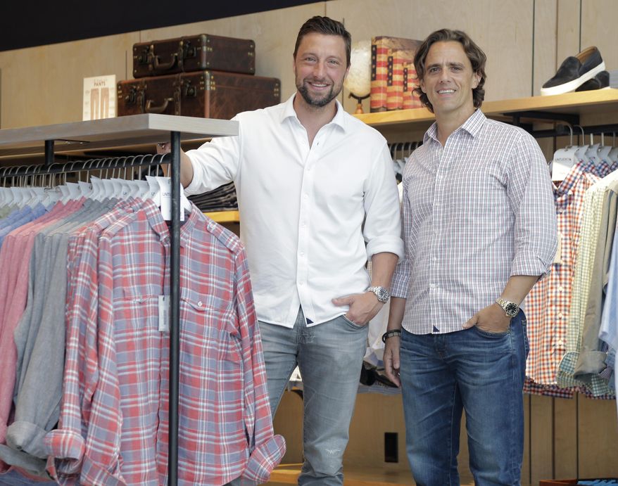 In this Aug. 8, 2018, photo UNTUCKit founder Chris Riccobono, left, and CEO Aaron Sanandres pose for a picture in one of their stores in New York. When Untuckit launched six years ago, it was hard to find a men’s shirt that could be worn untucked and didn’t look sloppy. Now the company is facing competition from the Gap, J. Crew and other stores that have started to sell shortened shirts. (AP Photo/Seth Wenig)