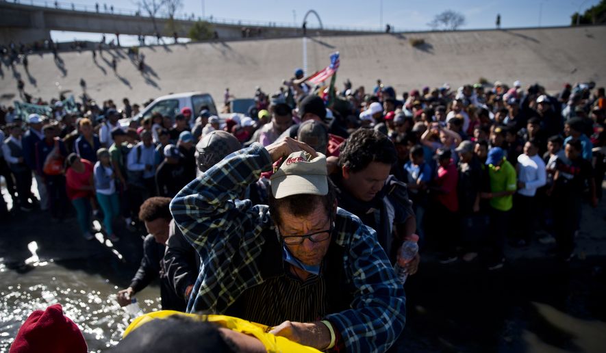 Migrants cross the river at the Mexico-U.S. border after pushing past a line of Mexican police at the Chaparral crossing in Tijuana, Mexico, Sunday, Nov. 25, 2018, as they try to reach the U.S. The mayor of Tijuana has declared a humanitarian crisis in his border city and says that he has asked the United Nations for aid to deal with the approximately 5,000 Central American migrants who have arrived in the city. (AP Photo/Ramon Espinosa)