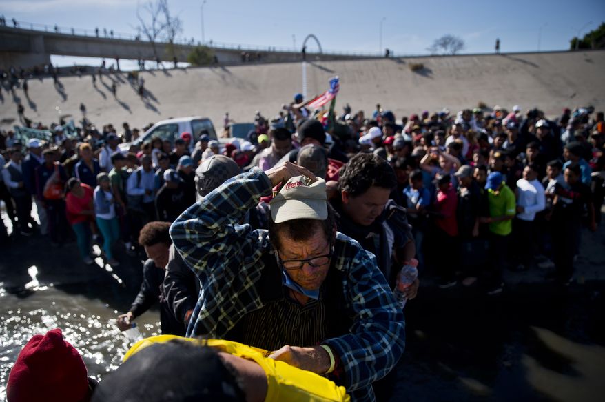 Migrants cross the river at the Mexico-U.S. border after pushing past a line of Mexican police at the Chaparral crossing in Tijuana, Mexico, Sunday, Nov. 25, 2018, as they try to reach the U.S. The mayor of Tijuana has declared a humanitarian crisis in his border city and says that he has asked the United Nations for aid to deal with the approximately 5,000 Central American migrants who have arrived in the city. (AP Photo/Ramon Espinosa)