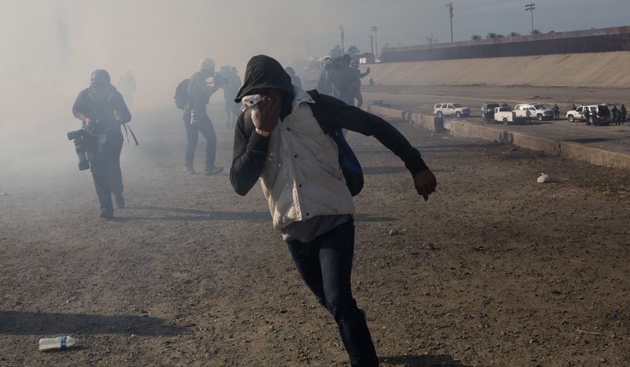 A migrant runs from tear gas launched by U.S. agents, amid members of the press covering the Mexico-U.S. border, after a group of migrants got past Mexican police at the Chaparral crossing in Tijuana, Mexico, Sunday, Nov. 25, 2018. The mayor of Tijuana has declared a humanitarian crisis in his border city and says that he has asked the United Nations for aid to deal with the approximately 5,000 Central American migrants who have arrived in the city.  (AP Photo/Rodrigo Abd)