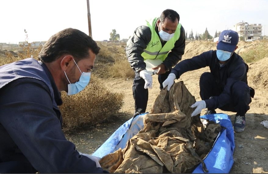 This frame grab from a video provided on Thursday, Nov. 22, 2018, shows a Syrian worker of a Raqqa group checking human remains at the site of a mass grave believed to contain the bodies of civilians and Islamic State militants, in Raqqa. A local official in the city of Raqqa says more than 500 bodies have so far been exhumed from one of the largest mass graves discovered in the city. The northern Syrian city was once the de facto capital of the Islamic State group and was liberated in a campaign that ended more than a year ago, but rescuers and early recovery teams continue to locate mass graves scattered around the city. (AP Photo)