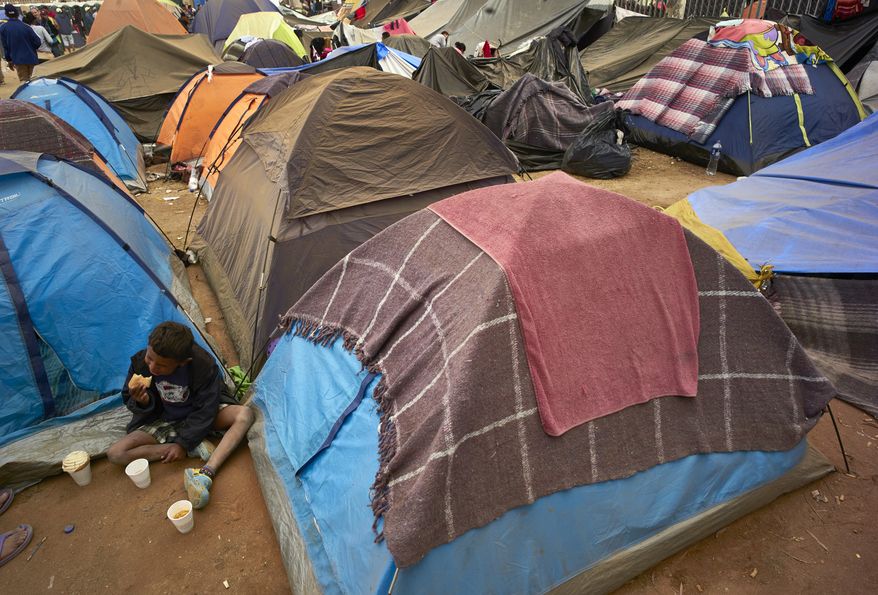 Darwin Dariel Paraon eats sitting next to a group of tents set up in a shelter for members of the migrant cavan, in Tijuana, Mexico, Wednesday, Nov. 28, 2018. As Mexico wrestles with what to do with more than 5,000 Central American migrants camped out at a sports complex in the border city of Tijuana, President-elect Andres Manuel Lopez Obrador&#x27;s government signaled Tuesday that it would be willing to house the migrants on Mexican soil while they apply for asylum in the United States — a key demand of U.S. President Donald Trump. (AP Photo/Gregory Bull)