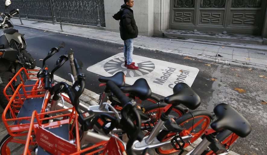 A tourist poses for a photo taken by another on a sign painted on the road indicating the boundary of the centre of the city in Madrid, Spain, Friday, Nov. 30, 2018. Madrid activated a new traffic restriction system Friday in an attempt to reduce pollution in the city. Petrol vehicles before 2000 and diesel ones registered before 2006 are banned from this central area but on the first day of the restrictions, drivers will not be fined as municipal police were only warning drivers of the new restrictions. (AP Photo/Paul White)