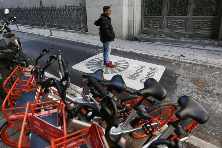 A tourist poses for a photo taken by another on a sign painted on the road indicating the boundary of the centre of the city in Madrid, Spain, Friday, Nov. 30, 2018. Madrid activated a new traffic restriction system Friday in an attempt to reduce pollution in the city. Petrol vehicles before 2000 and diesel ones registered before 2006 are banned from this central area but on the first day of the restrictions, drivers will not be fined as municipal police were only warning drivers of the new restrictions. (AP Photo/Paul White)