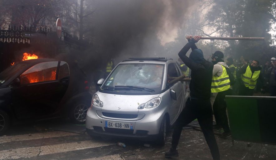 Hooded demonstrators smash a car during a demonstration Saturday, Dec.1, 2018 in Paris. Protesters angry about rising taxes clashed with French police for a third straight weekend and over 100 were arrested after pockets of demonstrators built barricades in the middle of streets in central Paris, lit fires and threw rocks at officers Saturday. (AP Photo/Thibault Camus)