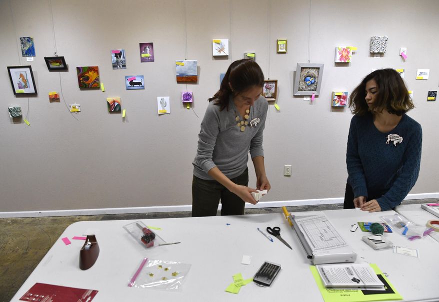 In this Nov. 7, 2018 photo, Laura Greenwood, left, the manager prepares the show "Tiny Art!" with the help of Hannah DeLeon at the 1818 Arthouse in Snyder, Texas. The Snyder gallery's show of small artwork will be up until Dec. 22. (Ronald W. Erdrich/The Abilene Reporter-News via AP)