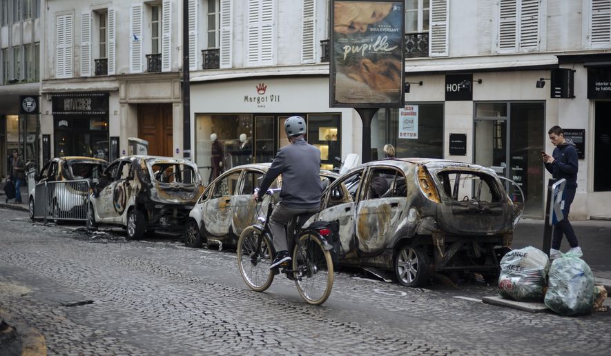 A man rides his bicycle past by charred cars, near the Arc de Triomphe, in Paris, Sunday, Dec. 2, 2018. A protest against rising taxes and the high cost of living turned into a riot in the French capital Saturday, as activists caused widespread damage and tagged the Arc de Triomphe with multi-colored graffiti during clashes with police. (AP Photo/Kamil Zihnioglu)
