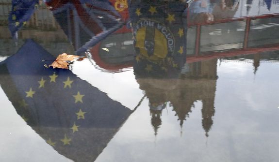 Protesters are reflected in a puddle as they wave European flags to demonstrate against Brexit in front of the Parliament in London, Monday, Dec. 3, 2018. British Prime Minister Theresa May is battling to persuade lawmakers to support the divorce agreement between Britain and the European Union in a Dec. 11 House of Commons vote. Opposition parties say they will vote against it, as do dozens of lawmakers from May&#39;s Conservatives. (AP Photo/Frank Augstein)