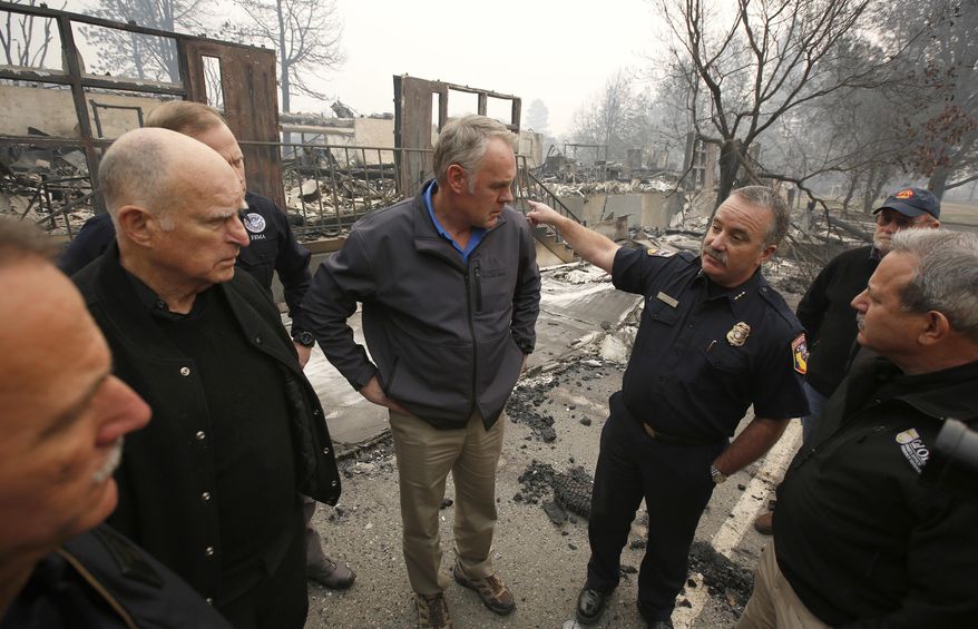 FILE - In a Nov. 14, 2018 file photo, Scott Upton, right, the chief of the Northern Region for the California Department of Forestry and Fire Protection briefs California Gov. Jerry Brown, second from left, Federal Emergency Management Agency Director Brock Long, third from left, and U.S. Secretary of the Interior Ryan Zinke, third from left, and Mark Ghilarducci, director of the Governor's Office of Emergency Services, right, look at the remains of Paradise Elementary school in Paradise, Calif. Monday Dec. 3 marks a return to school and some semblance of routine for thousands of children who lost their homes in the wildfire. (AP Photo/Rich Pedroncelli, File)