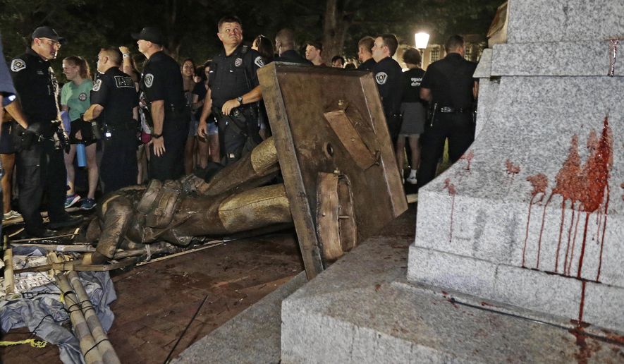 In this Aug. 20, 2018, file photo, police stand guard after the confederate statue known as Silent Sam was toppled by protesters on campus at the University of North Carolina in Chapel Hill, N.C. (AP Photo/Gerry Broome, File)