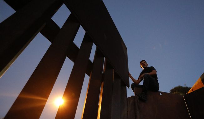 A man sits atop the U.S. border wall as he prepares to help other migrants climb over to San Ysidro, Calif., in order to surrender to the U.S. Border Patrol, in Playas de Tijuana, Mexico, Monday, Dec. 3, 2018. Thousands of Central American migrants who traveled with recent caravans want to seek asylum in the U.S. but face a decision between crossing illegally or waiting months, because the U.S. government only processes a limited number of those cases a day at the San Ysidro border crossing. (AP Photo/Rebecca Blackwell)