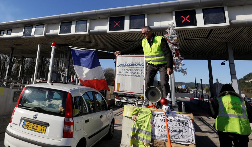 A demonstrator wearing a yellow vest waves a French flag as protesters open the toll gates on a motorway near Aix-en-Provence, southeastern France, Tuesday, Dec. 4, 2018. French Prime Minister Edouard Philippe announced a suspension of fuel tax hikes Tuesday, a major U-turn in an effort to appease a protest movement that has radicalized and plunged Paris into chaos last weekend. (AP Photo/Claude Paris)