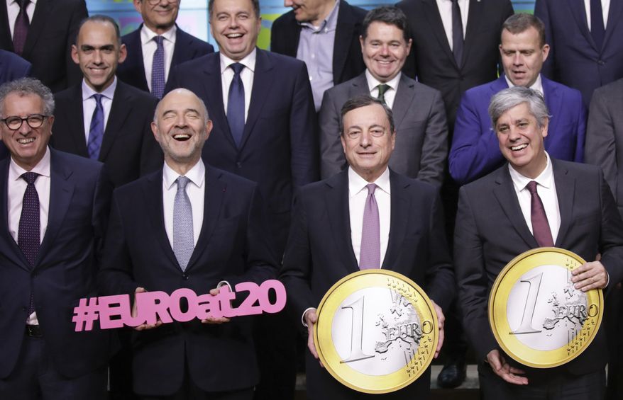 European Central Bank President Mario Draghi, front second right, and Portuguese Economy Minister Mario Centeno, center right, hold giant euro coins during a group photo of EU finance ministers in Brussels, Monday, Dec. 3, 2018. The euro celebrates 20 years of being in use in January of 2019. At front left is Luxembourg's Finance Minister Pierre Gramegna and second left is European Commissioner for Economic and Financial Affairs Pierre Moscovici. (AP Photo/Olivier Matthys)