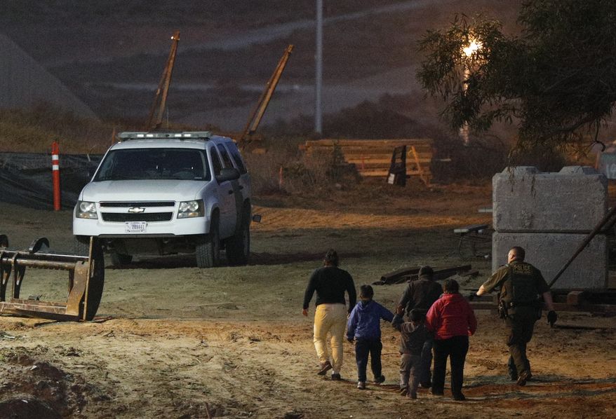 Migrants are escorted by a U.S. Border Patrol agent as they are detained after climbing over the border wall from Playas de Tijuana, Mexico, to San Ysidro, Calif., Monday, Dec. 3, 2018. Thousands of Central American migrants who traveled with recent caravans want to seek asylum in the U.S. but face a decision between crossing illegally or waiting months, because the U.S. government only processes a limited number of those cases a day at the San Ysidro border crossing. (AP Photo/Rebecca Blackwell)