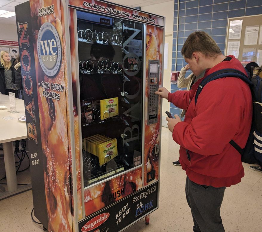 This Dec. 7, 2018 photo shows Ohio State University sophomore Nick Vales buys a package of bacon slices from a vending machine available on the Columbus campus. The machine offers cooked bacon strips and bacon bits for $1.The Ohio Pork Council sponsored the machine, and it received bacon donations from Smithfield, Hormel and Sugardale. Proceeds from the machine will go toward Ohio State's meat science program. [JD Malone/The Columbus Dispatch via AP)