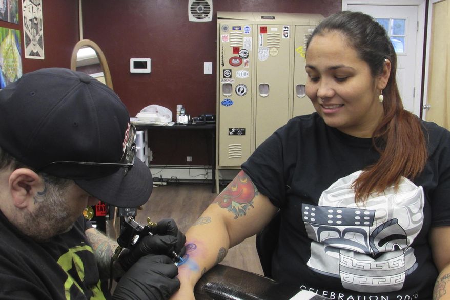 In this photo taken Nov. 30, 2018, "Salty" Jack Reed Jr. puts the finishing touches on Davina Cole's formline semicolon tattoo at Taku Tattoo in Juneau, Alaska. At Taku Tattoo recently business card-sized tattoos were $50 with half of the proceeds going toward Juneau Suicide Prevention Coalition. (Ben Hohenstatt/The Juneau Empire via AP)