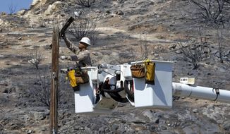FILE - In this June 27, 2016 file photo, Robert Delgado, a lineman for Southern California Edison, works on a power line at fire ravaged South Lake, Calif. SCE wants to spend $582 million to cover some power lines and deploy cameras in areas at high risk for wildfires. Officials from the utility shared plans with legislative staff on Monday, Dec. 10, 2018 as the utility works on clean up and repair from the Woolsey Fire last month. (AP Photo/Rich Pedroncelli, File)