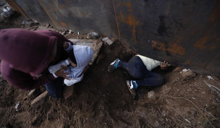 Honduran migrant Joel Mendez, 22, feeds his eight-month-old son Daniel as his partner Yesenia Martinez, 24, crawls through a hole under the U.S. border wall, in Tijuana, Mexico, Friday, Dec. 7, 2018. Moments later Martinez surrendered to waiting border guards while Mendez stayed behind in Tijuana to work, saying he feared he'd be deported if he crossed. (AP Photo/Rebecca Blackwell)
