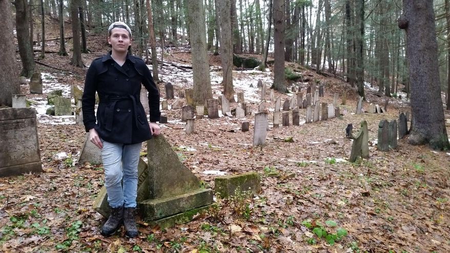 In this Nov. 2018 photo, Tom Vaughn, 20, of Plymouth, Conn., poses at Hillside Cemetery in Thomaston, Conn, which he is voluntarily cleaning up. Vaughn found in May that many of the 200-plus headstones had either fallen down or were knocked down. Not all stones were placed in the right spots, despite the town having kept excellent records of those buried in town. (Kurt Moffett/Republican-American via AP)